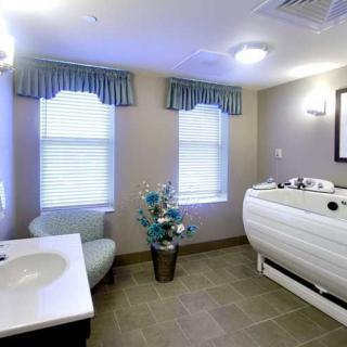A modern bathroom with a bathtub, sink, tiled floor, and two windows with curtains.