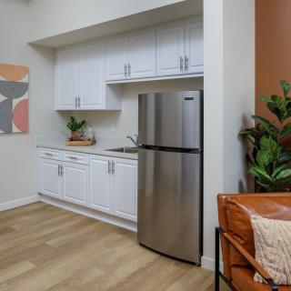 A modern apartment kitchen with white cabinets, stainless steel fridge, and wood flooring.