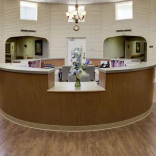 A well-organized reception area with a central desk, chandelier lighting, and decorative flowers.