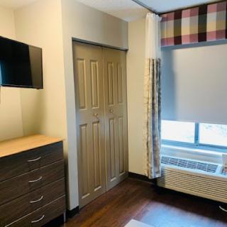 A cozy and modern room featuring a TV, dresser, and window with curtains.