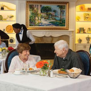 An elderly couple enjoys a meal together at a restaurant, smiling and engaged in conversation amidst a warm and inviting atmosphere.