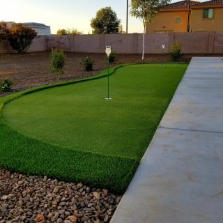A backyard putting green with artificial grass next to a concrete area.