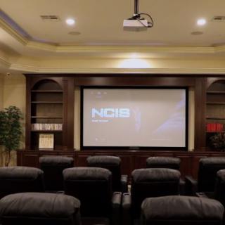 A cozy home theater setup with comfortable seating and a large screen displaying 'NCIS'.