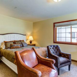 A cozy bedroom featuring a large bed, two leather chairs, and a window that lets in natural light.