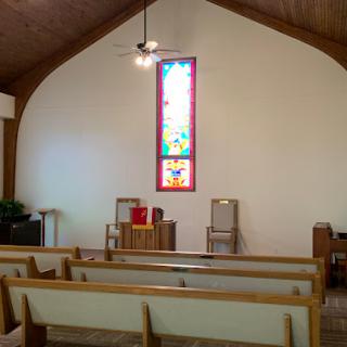 The interior of a cozy church featuring wooden pews and a colorful stained glass window.