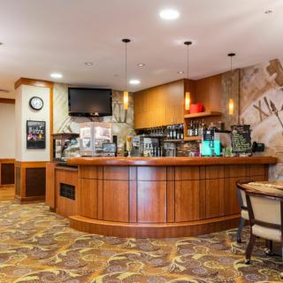 A cozy coffee shop interior featuring a wooden counter with various beverages, stylish lighting, and comfortable seating.