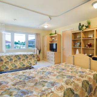 A cozy bedroom featuring a bed with floral-patterned bedding, wooden shelves, and a television.