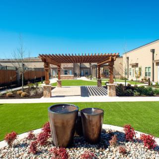 A beautifully landscaped garden with a pergola and water features under a clear blue sky.