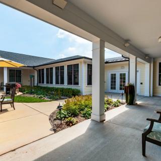 A serene courtyard with benches and outdoor seating, surrounded by a garden and framed by a building's columns.