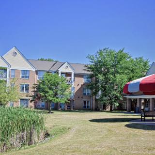 A residential building with a well-maintained lawn, surrounded by trees and featuring a gazebo under a clear blue sky.