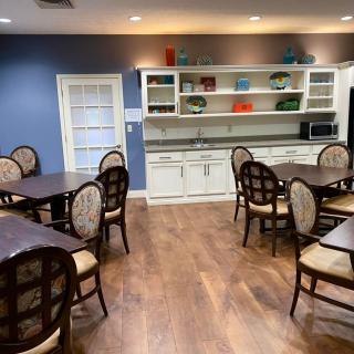 A well-lit dining room with tables, chairs, and a kitchen area featuring open shelves.