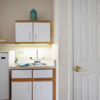 Compact kitchenette with white cabinets and a small fridge.