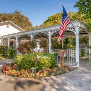 A beautifully landscaped garden features a white gazebo with an American flag, surrounded by vibrant flowers and a central fountain.
