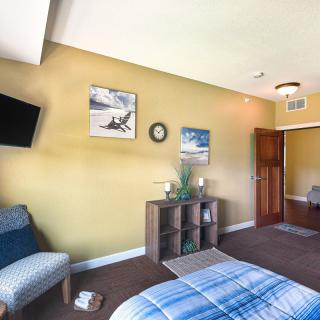A cozy bedroom with green walls, featuring a bed, chair, wall-mounted TV, and decorative elements.