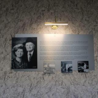 A historical plaque featuring a black and white photograph of a couple, accompanied by descriptive text and additional small images, illuminated by overhead lighting.