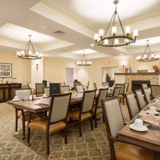 An elegant dining room with multiple tables and chairs, adorned with chandeliers and warm lighting.