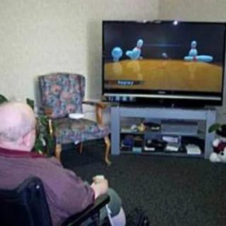 An elderly person in a wheelchair playing a video game on television.