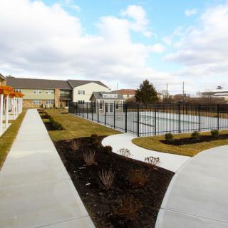 A view of outdoor tennis courts surrounded by pathways and buildings under a partly cloudy sky.