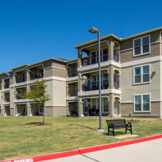 A modern apartment building with multiple balconies and a well-kept lawn under a clear blue sky.