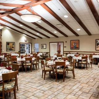 An empty restaurant dining room with neatly arranged tables and chairs, featuring wooden beams on the ceiling.