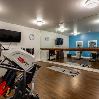A modern gym room featuring exercise equipment, mirrors, and a wooden floor.