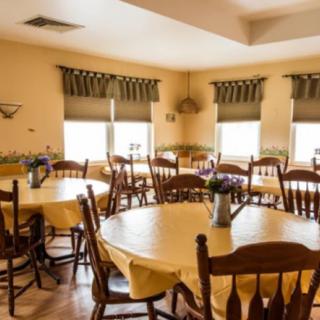 A cozy dining room with round tables, wooden chairs, and windows adorned with curtains.