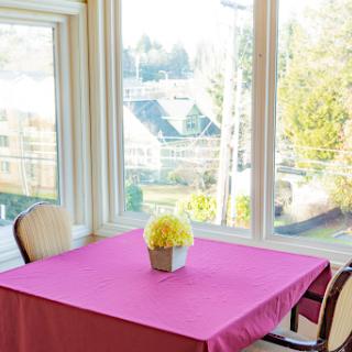 A bright and inviting dining area with a pink tablecloth and a floral centerpiece, showcasing a beautiful view through the windows.