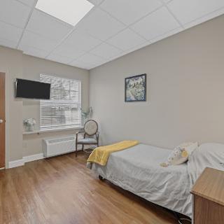 A cozy bedroom featuring a bed, a small table, and a television, complemented by natural light from the window.