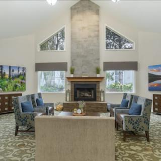 A spacious living room with a central fireplace surrounded by comfortable armchairs and large windows providing natural light.