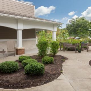 A well-maintained garden area with a patio, featuring neatly trimmed bushes and benches for seating.