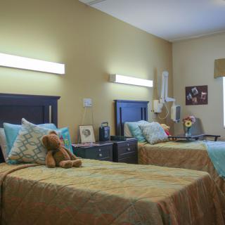 A cozy bedroom with twin beds adorned with patterned bedspreads and a teddy bear on one of the pillows, featuring decorative wall art and a nightstand between the beds.