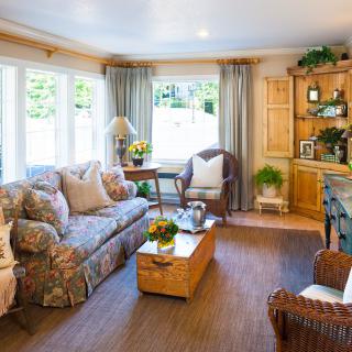 A cozy living room with a floral sofa, wooden coffee table, and large windows adorned with curtains.
