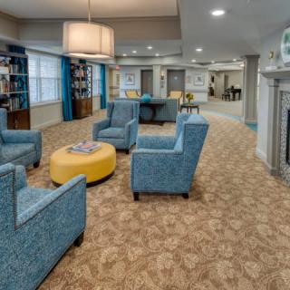 A modern living room with blue chairs, a yellow ottoman, and bookshelves.