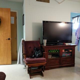 A cozy living room setting featuring a wooden chair, a television on a cabinet, and a door.