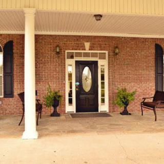 A welcoming front porch with brick exterior, featuring a stylish black door flanked by two benches and potted plants.