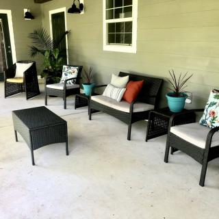 A cozy patio setup with outdoor furniture, including chairs, a sofa, a table, and decorative plants.