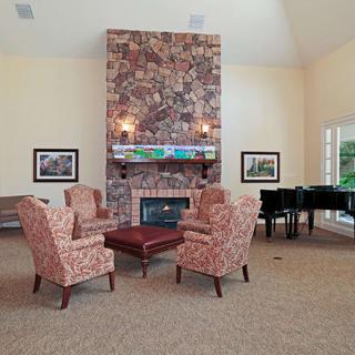 A cozy living room with armchairs around a fireplace and a piano in the corner.