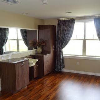 A well-lit interior room featuring a vanity, large windows with curtains, and polished wooden flooring.