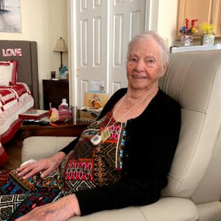 An elderly woman smiles warmly while sitting comfortably in her home.