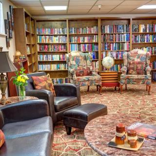 A cozy library lounge featuring armchairs and bookshelves filled with books.