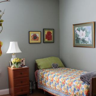 A cozy bedroom corner with a single bed, floral quilt, and decorative artwork on the walls.
