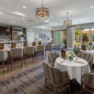 An elegant restaurant interior featuring a bar and multiple dining areas with stylish chandeliers and neatly arranged tables.