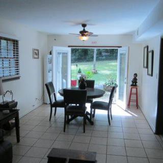 A bright dining room with tile flooring, featuring a table and chairs, large windows, and a ceiling fan.