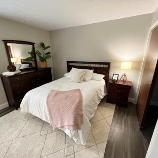 A cozy bedroom with a neatly made bed, dark wood furniture, and soft lighting.