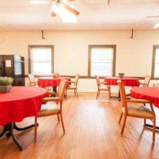 A brightly lit dining area with red tablecloths on the tables and wooden chairs arranged around them.