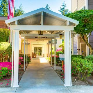 A covered walkway leading to the entrance of a building, surrounded by lush landscaping.