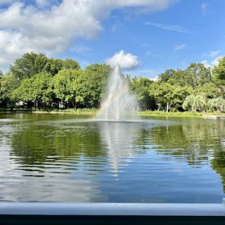 A serene park view featuring a fountain surrounded by lush greenery and a clear blue sky.