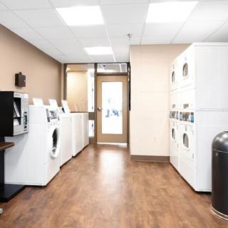 A modern laundry room with multiple washing machines and dryers lined up against the walls.