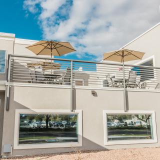 A modern building with a balcony featuring outdoor seating and umbrellas under a blue sky.