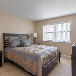 A simple and cozy bedroom with a neatly made bed, bedside lamp, and window blinds.